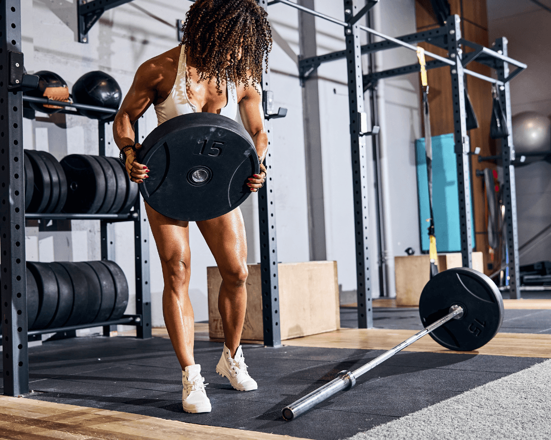 Female weightlifter loading barbell with weight plate in gym